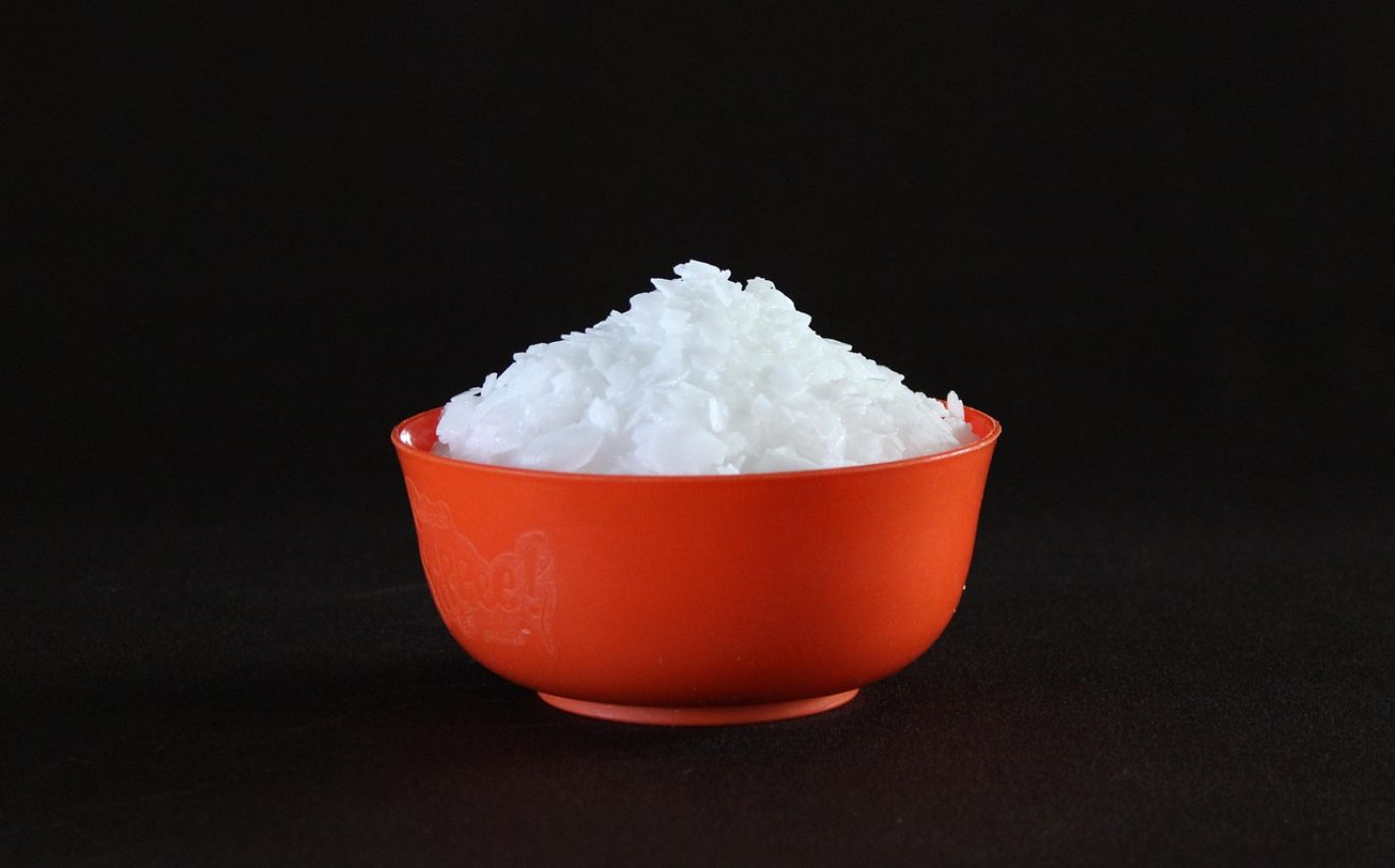A close-up of Solvay Caustic Soda pellets or flakes, symbolizing industrial chemical supply for manufacturing processes